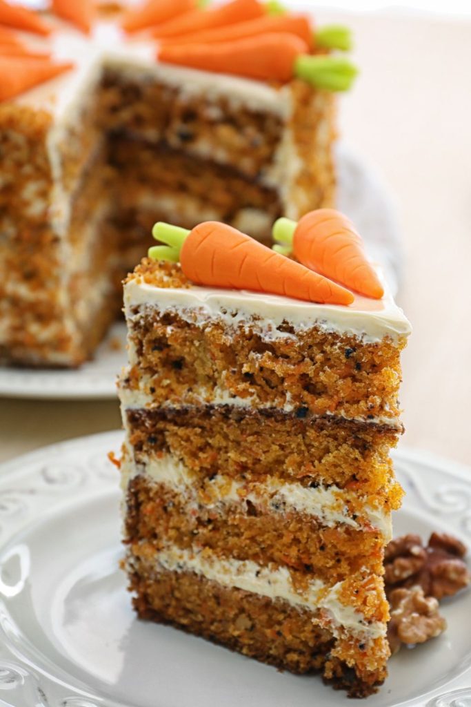 This is a slice of carrot cake on a plate with carrot cake in the background.