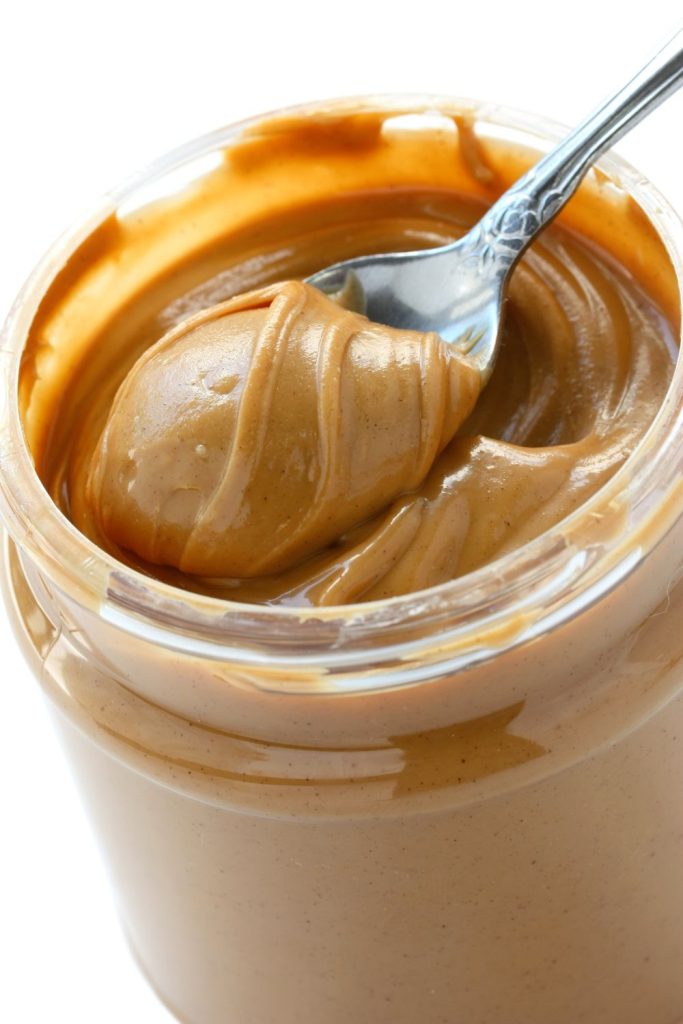 This is an open jar of peanut butter with a spoon.