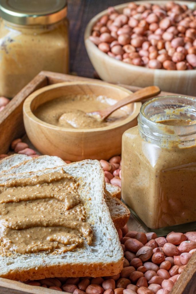 This is peanut butter in a jar, peanut butter in a bowl, peanut butter on a slice of bread, and a bowl of peanuts.